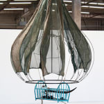 An image of a teardrop shaped steel sculpture with a framed baby crib made out of wood, glass, silver leaf, cowrie shells, sea shells, taxidermy eyes, vintage saris