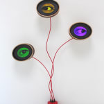 Small red cylinder with three red wires and three round monitors displaying blinking eyes in different colors.