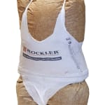 Sculpture of a torso made from a brown paper bag filled with urethane foam. Covering the paper bag is a white shopping bag cut up in a way to mimic a spaghetti strap top and thong underwear. The text on the shopping bag reads Rockler Woodworking and Hardware