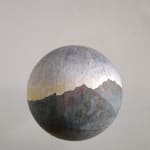 Ballpoint pen drawing with washes of brown blue yellow and green watercolor create a mountainous sunrise landscape on paper which is pasted onto a large fiberglass hanging globe