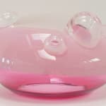 UFO-shaped glass sculpture. Top 2/3 opaque blush-pink, bottom 1/3 pink. Clear top with clear bubbles of varying sizes.