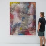A man stands to the right and faces a multicolored, brightly colored abstract painting.
