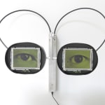 Two rectangular monitors displaying green/yellow eyes with wandering eyes. The monitors are in black rubber circles and are connected to silver metal bar that is mounted to wall by two rounded rubber wires.