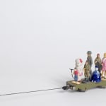 Still from video; group of figurines stand on a platform that is being pulled to the left by a thin black string