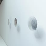 Side view of three reflective disks mounted in a row on a white wall.