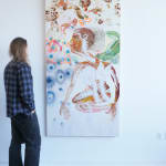 A man admires a painting of a brown skinned person kneeling, surrounded by multicolored nature imagery.