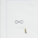 Figurine draws comparatively massive infinity sign in pencil on lined paper, below a similarly sized infinity sign in black ink
