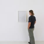 A man stands to the right of and faces a framed and hanging 5x8 grid of rectangular foil slides.