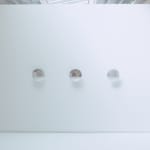 Distanced view of three reflective disks mounted in a row on a white wall.
