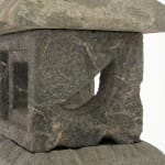 Detail view of stone lantern with square body with holes in center.