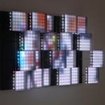 Still image of multiple colorful LEDs behind multiple squares of sandblasted glass which are mounted at various depths from the wall The LEDs display a blurred city street scene