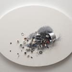 Assemblage of multiple tiny found objects and gray silver glitter spilling out from a small metallic tipped over bucket pasted onto a white oval canvas