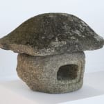 Weathered stone sculpture with open hole in center and sloped edge topper.
