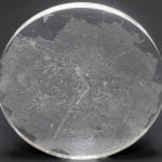 A clear convex disk with etchings set on a dark grey background.