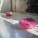 Two pink glass blown sculptures arranged on a white floor.