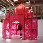 An image of a reddish pink plastic sculpture piece with a wooden chair and materials that embrace love.