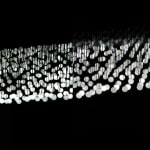 Still image of multiple spread out white LEDs mounted at the ends of wires and placed inside incandescent bulbs hang and extend out in three dimensions at different lengths to form the shape of waves. The LEDs display scenes of waves moving