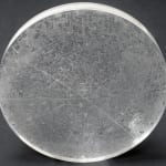 A clear disk with etchings on a dark grey background.