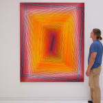 A man admires a painting of overlapping, radiating, neon rectangles.