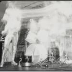 Black and white photograph of a punk rock group performing at a concert In the scene several members of the group are playing instruments but are highly distorted in a way that makes it look like they are evaporating into glowing vapors