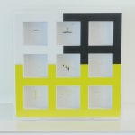 Plexiglass box with a grid of 9 clear windows. Border colors: White, upper left third; Black, upper right two-thirds; Neon yellow, bottom half.