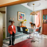 White boy in red blazer standing contemplatively in kitchen with dog on table and Black Jesus portrait on wall by Ron Norsworthy
