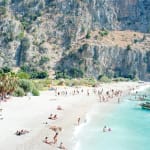 Beachgoers relaxing by the ocean with cliffs in background in Butterfly Valley, Turkey, by Massimo Vitali