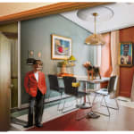 White boy in red blazer standing contemplatively in kitchen with dog on table and Black Jesus portrait on wall by Ron Norsworthy