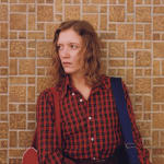 Ginger Shore wearing red plaid shirt against brick wall by Stephen Shore