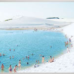 People swim and relax in a bright blue lagoon surrounded by white sand dunes; photograph by Massimo Vitali.