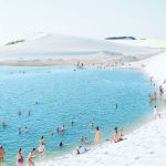 People swim and relax in a bright blue lagoon surrounded by white sand dunes; photograph by Massimo Vitali.