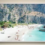 Beachgoers relaxing by the ocean with cliffs in background in Butterfly Valley, Turkey, by Massimo Vitali
