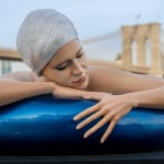 A large sculpture of a white woman in an blue innertube with a Swarovski crystal cap, a city and bridge are in the background. It's New York.