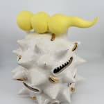 Ceramic sculpture “Fat white spooter” by Kartini Thomas, side view showing spiked white surface with golden details and gaping mouths.