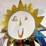 Large mixed media artwork, by British sculptor Andrew Logan. A gold mirrored sun shape expressing a smile, creating a joyful impression.