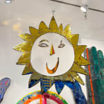 Large mixed media artwork, by British sculptor Andrew Logan. A gold mirrored sun shape expressing a smile, creating a joyful impression.