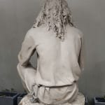 A clay model of the statue during the sculpting process, showcasing the intricate details of Jesus' back and hair before the casting stage, with a neutral gray background.