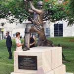 The bronze statue of Allan Border at The Gabba in Brisbane depicts the cricketer mid-swing in an iconic pose. The intricate details of the bat, pads, and uniform celebrate his legacy. The statue is mounted on a sandstone base with a commemorative plaque, surrounded by greenery and people at the unveiling event.