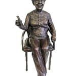 A front-facing view of the bronze statuette of Audrey, showing her seated with her legs crossed. She holds a book in her left hand, and her facial expression is cheerful and lively, capturing her engaged demeanor. The intricate details of her clothing and chair are clearly visible.