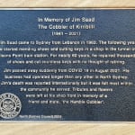 A memorial plaque dedicated to Jim Saad, known as "The Cobbler of Kirribilli," recounting his journey from Lebanon to Sydney in 1962. The plaque details his nearly 60-year career repairing shoes and cutting keys at Milsons Point train station, his passing due to COVID-19 in 2021, and his impact on the local community.