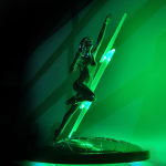 A sleek, futuristic silver trophy illuminated with green light. The design features a dynamic human figure in a leaping pose, reaching upward, with a glowing green lightning bolt cutting through the sculpture diagonally. The base of the trophy depicts a polished map of the globe.