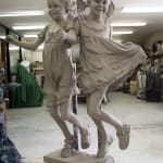Clay sculpture in progress in the studio of two young girls holding hands and skipping, capturing movement and joy, part of the Expressions of Love series.