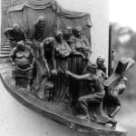 A bronze relief sculpture depicting Station VIII of the Stations of the Cross, titled 'Jesus Speaks to the Women of Jerusalem.' The scene features Jesus kneeling under the weight of the cross, reaching out to a group of women and children gathered before him. The women, dressed in flowing garments, display varied expressions of sorrow and concern. The background includes draped fabric and architectural elements, adding depth and context to the scene. The intricate details capture the emotional exchange between Jesus and the women during his journey to Calvary.