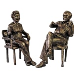 A bronze statuette titled Audrey and Norman depicting an elderly couple in a lively and warm interaction. Audrey sits in an armchair, relaxed and smiling, while Norman, seated in a simple chair, animatedly gestures with a pair of glasses in hand. The sculpture captures a moment of joy and connection between the two.