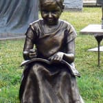 Bronze statue of a young girl seated on grass, focused on reading a book in her lap, part of the 'Expressions of Love' series at Hunter Valley Gardens.