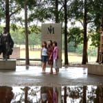 Two bronze graduate statues at Macquarie University, featuring a male graduate walking forward and a female graduate joyfully raising her mortarboard in celebration. The statues are surrounded by tall trees, adding to the inspirational atmosphere.