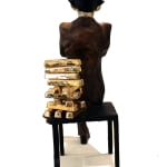 Rear view of a large banker sculpture showing the back of the seated figure. The chair's backrest is made of stacked gold bullion bars, symbolizing wealth, with one chair leg bending under the weight. The sculpture's polished, reflective head contrasts with the textured bronze finish of the suit, highlighting its intricate details.