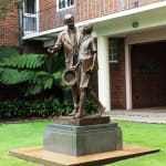 A side perspective of the Shore Boys bronze statue, highlighting the dynamic interaction between the two figures. The setting, with the school's red brick building in the background, complements the statue's theme of education and legacy.
