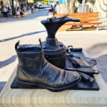 A bronze still-life sculpture commemorating Jim Saad, featuring a cobbler's toolkit including a shoe last, a worn leather boot, scissors, a hammer, and other tools. The artwork reflects the craft and legacy of Jim's dedication to his work.