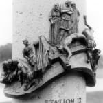 bronze relief sculpture depicting Station IX of the Stations of the Cross, where Jesus is nailed to the cross. The intricate details include Roman soldiers performing the crucifixion, mourners in grief, and a dynamic composition of anguish and reverence. The relief is mounted on a cylindrical structure with the inscription 'STATION IX' below.